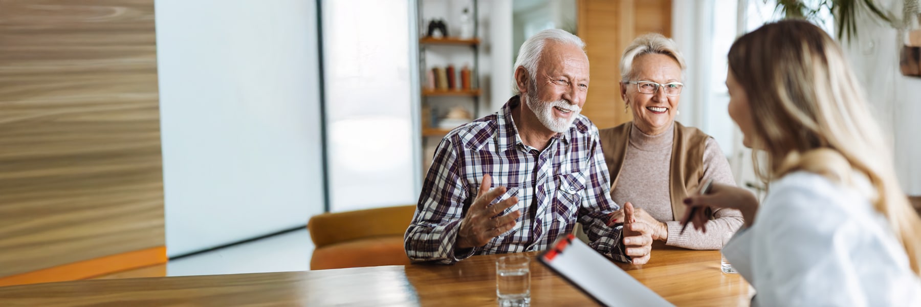 Elderly couple smiling and conversing with a woman holding a clipboard.