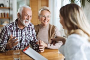 Elderly couple smiling and conversing with a woman holding a clipboard.